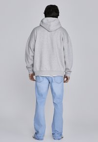 Sivá mikina s kapucňou, s voľným strihom a spustenými ramenami, skombinovaná s svetlomodrými džínsami. Mäkka textúra, voľný dizajn.