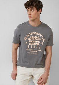 Grijze katoenen t-shirt met korte mouwen en een grote roze grafische print. Gladde textuur, klassiek ronde hals ontwerp, lichtgewicht stof.