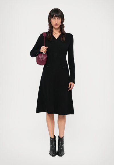 Mustat neulemekot pitkillä hihoilla, V-pääntiellä, levenevällä helmalla ja sivutaskuilla. Yhdistetty mustien nilkkureiden kanssa, joissa on hopeaa yksityiskohtaa, ja maroonin värisen käsilaukun kanssa.