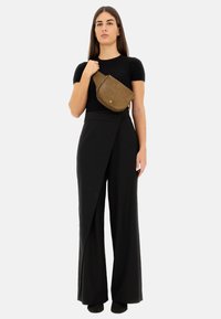 Top nero aderente, pantaloni neri a vita alta con design asimmetrico a drappo e una borsa a tracolla in pelle marrone con motivo a foglia.