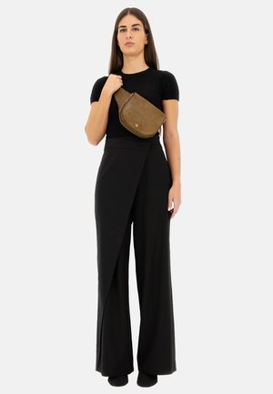 Top nero aderente, pantaloni neri a vita alta con design asimmetrico a drappo e una borsa a tracolla in pelle marrone con motivo a foglia.