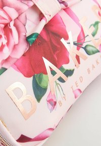 Kosmetična torbica s cvetnim vzorcem iz teksturirane tkanine, ki prikazuje rožnate vrtnice, zelene liste in rožnato zlato besedilo, ki pravi "BAKER by TED BAKER."