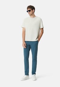 Lichtgrijze t-shirt met korte mouwen, teal slim-fit broek, witte sneakers en zwarte zonnebril. Eenvoudig ontwerp met een casual pasvorm.