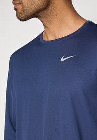 Μπλούζα μακρυμάνικη σε ναυτικό μπλε χρώμα, φτιαγμένη από υφασμάτινη υφή, με μικρό ασημένιο λογότυπο Nike στο επάνω αριστερό μέρος του στήθους.