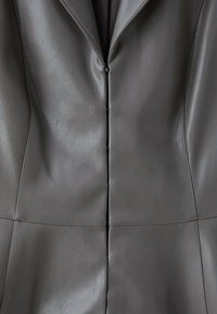 Gros plan sur le devant d'une veste en cuir grise montrant une fermeture à boutons cachée et des détails de coutures ajustées.
