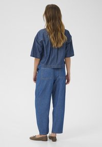 Denimoutfit vist fra ryggen, der inkluderer en løstsiddende, kortærmet top og lige ben bukser, begge i mellemblå med synlige sømme.