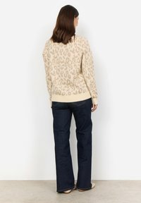 Beige leopardmönstrad tröja med ribbat avslut och muddar, ihopparad med mörkblå utsvängda jeans, visad bakifrån mot en neutral bakgrund.
