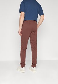 Bruna träningsbyxor med en avsmalnande passform, dragsko i midjan, sidostängningar och ribbade muddar. Bärs tillsammans med en marinblå t-shirt och vita sneakers.