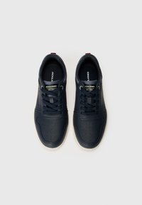 Navy blå sneakers med en glatt skinnfinish, med perforeringer, snørebånd og merke på tungen, satt mot en enkel bakgrunn.