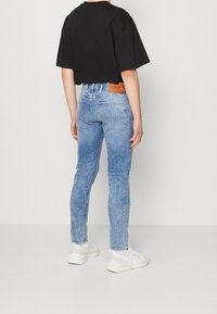 Schmale blaue Denim-Jeans mit einem ausgewaschenen Finish, fünf Taschen, Lederpatch auf der Rückseite und einem schwarzen, verkürzten T-Shirt. Weiße Sneaker mit Akzenten.