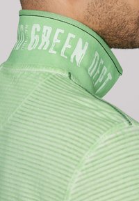 Zelený golier s riasenou textúrou a nápisom "GREEN DEPT" potlačeným bielej farbe. Má štruktúrovaný vzor a kontrastné čierne stehy.