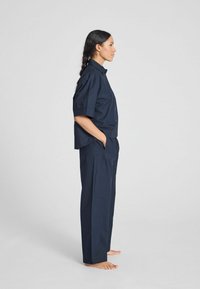 Camicia di cotone blu navy a maniche corte con vestibilità rilassata, abbinata a pantaloni a vita alta coordinati. Texture liscia e design minimalista.