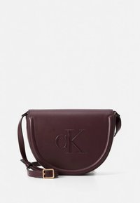 Bordeauxrode leren crossbodytas met een gebogen vorm, geperst "cK"-logo, verstelbare riem en hardware in goudkleur.
