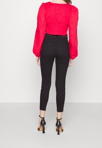 Top corto rojo de manga larga con mangas abullonadas, combinado con jeans skinny negros y zapatos de tacón alto negros. Tejido suave, diseño ajustado.