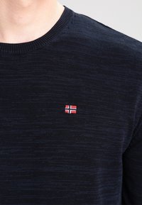 Maglione blu navy lavorato a maglia con scollo rotondo, caratterizzato da una piccola bandiera norvegese ricamata sull'area del petto sinistro. Tessuto morbido e peso medio.