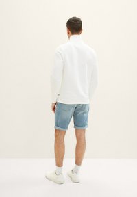Suéter blanco de manga larga con cuello alto, combinado con pantalones cortos de mezclilla claros enrollados y zapatillas blancas. Diseño sencillo, estilo casual.