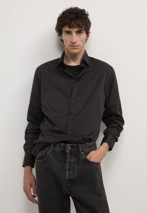 Schwarzes Hemd mit Knöpfen, das eine glatte Textur und lange Ärmel hat, kombiniert mit dunkelblauen Jeans aus Denim mit klassischem Fünf-Taschen-Design.