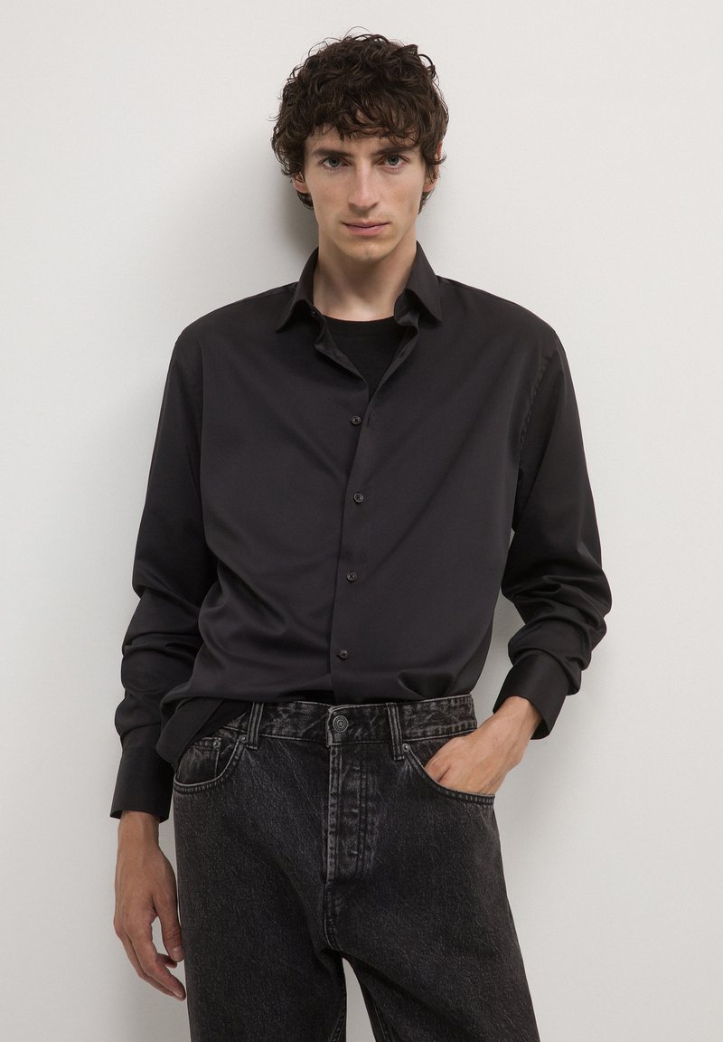 Camicia nera con bottoni, dal tessuto liscio e maniche lunghe, abbinata a jeans denim scuri con un design classico a cinque tasche.