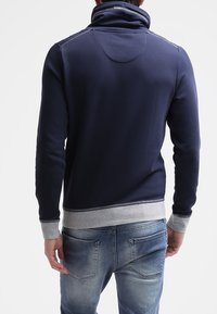 Felpa blu navy con colletto alto, polsini a coste grigi e una texture di tessuto liscia. Presenta dettagli di cucitura alle spalle e all'orlo.