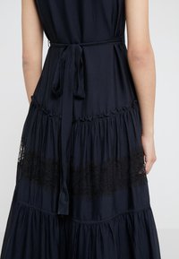 Robe noire sans manches avec ceinture à la taille, tissu texturé et panneau en dentelle à mi-longueur, vue de dos sur une personne.