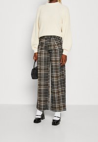 Krämfärgad stickad tröja med raglanärmar, kombinerad med vida rutiga byxor i brun, svart och vit. Accessoarer inkluderar en liten svart handväska.