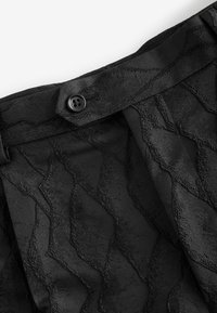 Black fabric with wave-patterned texture and smooth finish. Features a button closure at the waistband for secure fastening.