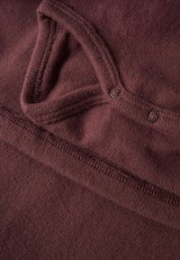 Burgundia lõngakangas, millel on sile tekstuur, ümara kaelusega ja kahe metallist nööbiga. Äärtes on nähtav õmbluse detail.