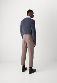 Pull en laine bleu marine avec une texture côtelée, associé à un pantalon beige clair et des bottines noires. Design minimaliste aux lignes épurées.
