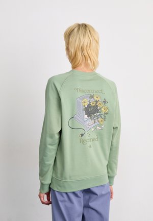 Grønn hettegenser med lange ermer, rund hals og et grafisk motiv av en datamaskin med blomster. Teksten sier "Koble fra for å koble til igjen." Myk tekstur.