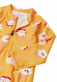 Gelbes Schwimmoberteil mit floralem Design, ausgestattet mit langen Ärmeln, einem halben Reißverschluss vorne und einem glatten, elastischen Stoff. Akzente in Pink und Weiß.