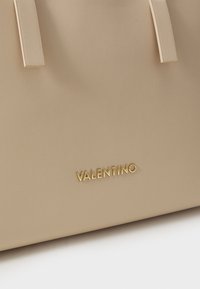 Bež torba od kože sa glatkom teksturom, s zlatnim "VALENTINO" logotipom. Dva gornja držača za nošenje. Jednostavan i elegantan dizajn.