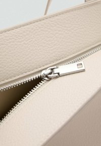 Bolso de piel beige con un acabado texturizado, que presenta un zipper plateado y un detalle de tirador, parcialmente abierto para revelar el interior.
