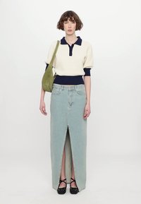 Pull en maille ivoire avec col marine, associé à une jupe maxi en denim bleu clair avec une fente avant, et un sac à épaule vert olive. Chaussures noires.
