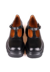 Chaussures Mary Jane en cuir noir avec semelles en caoutchouc épaisses et sangles à boucle, vues de face sur un fond blanc.