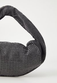 Svart tyghandväska med en texturerad, böjd form. Har silverfärgade nitar i ett prickmönster och ett tjockt, vadderat bärhandtag.