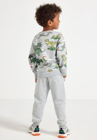 Gray sweatshirt with a dinosaur print on the back, paired with gray sweatpants. Sneakers have a black and white design with orange accents.