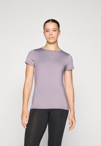 Short-sleeved, fitted t-shirt in light purple fabric, featuring a round neckline and subtle logo detail on the chest, paired with black leggings.