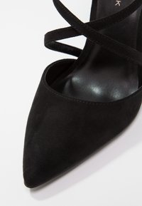 Black suede pointed-toe high heel with thin crisscross straps over the foot and a smooth leather insole.