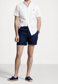 White short-sleeve button-up shirt, navy drawstring shorts, and navy espadrilles with a logo. Smooth fabric, casual fit, knee-length shorts.