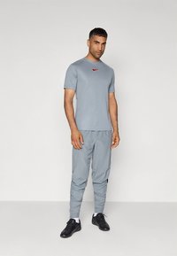 Hall hall spordiriietus, mis koosneb lühikeste varrukatega topist ja kitsenevate pükstega, valmistatud kergest kangast, millel on väike punane Nike logo. Mustad kingad.