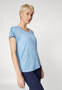 Lys blå V-hals t-skjorte med korte ermer, med et diskret blomstermønster og en jevn, myk tekstur. Kombinert med mørke leggings.