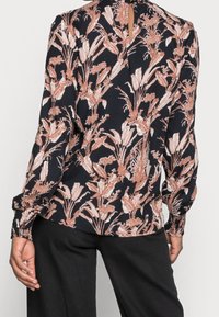 Blouse à motif floral en tissu bleu marine foncé avec des motifs botaniques rose clair et crème, manches longues et détail de fermeture boutonnée au dos.