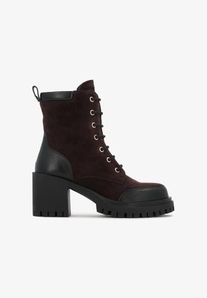 Braune Wildleder-Stiefeletten mit schwarzen Lederakzenten, goldenen Ösen, einem klobigen schwarzen Absatz und einer profilierten Sohle, die ein Schnürdesign haben.