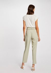 Lichtgrijze t-shirt met cap sleeves, gecombineerd met hoog-vaste, lichtgroene broek met een elastische tailleband en zijzakken.