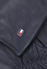 Navy leather fabric with a textured surface, featuring a rectangular metal badge in colors black, white, and red.