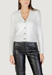 Cardigan bianco a coste con scollatura a V, dotato di cinque bottoni decorativi e un orlo peloso. Abbinato a pantaloni neri di pelle.