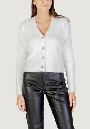 Cardigan blanc côtelé avec un col en V, doté de cinq boutons décoratifs et d'un ourlet duveteux. Associé à un pantalon en cuir noir.