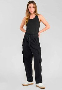 Zwarte cargobroek met een verstelbare tailleband, voorzien van meerdere zijzakken. Gecombineerd met een zwart tanktop en witte sneakers.