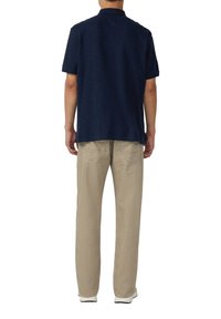 Granatowa koszulka polo wykonana z miękkiego materiału, z luźnym krojem, krótkimi rękawami i stójką, w połączeniu z jasnobeżowymi spodniami.