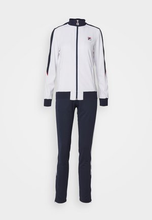 Giacca bianca con zip e accenti blu navy, abbinata a pantaloni sportivi blu navy con strisce laterali e zip sui polsini.